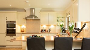 Una cocina moderna con gabinetes blancos, una campana extractora de acero inoxidable, un horno doble e isla de madera con taburetes de bar.