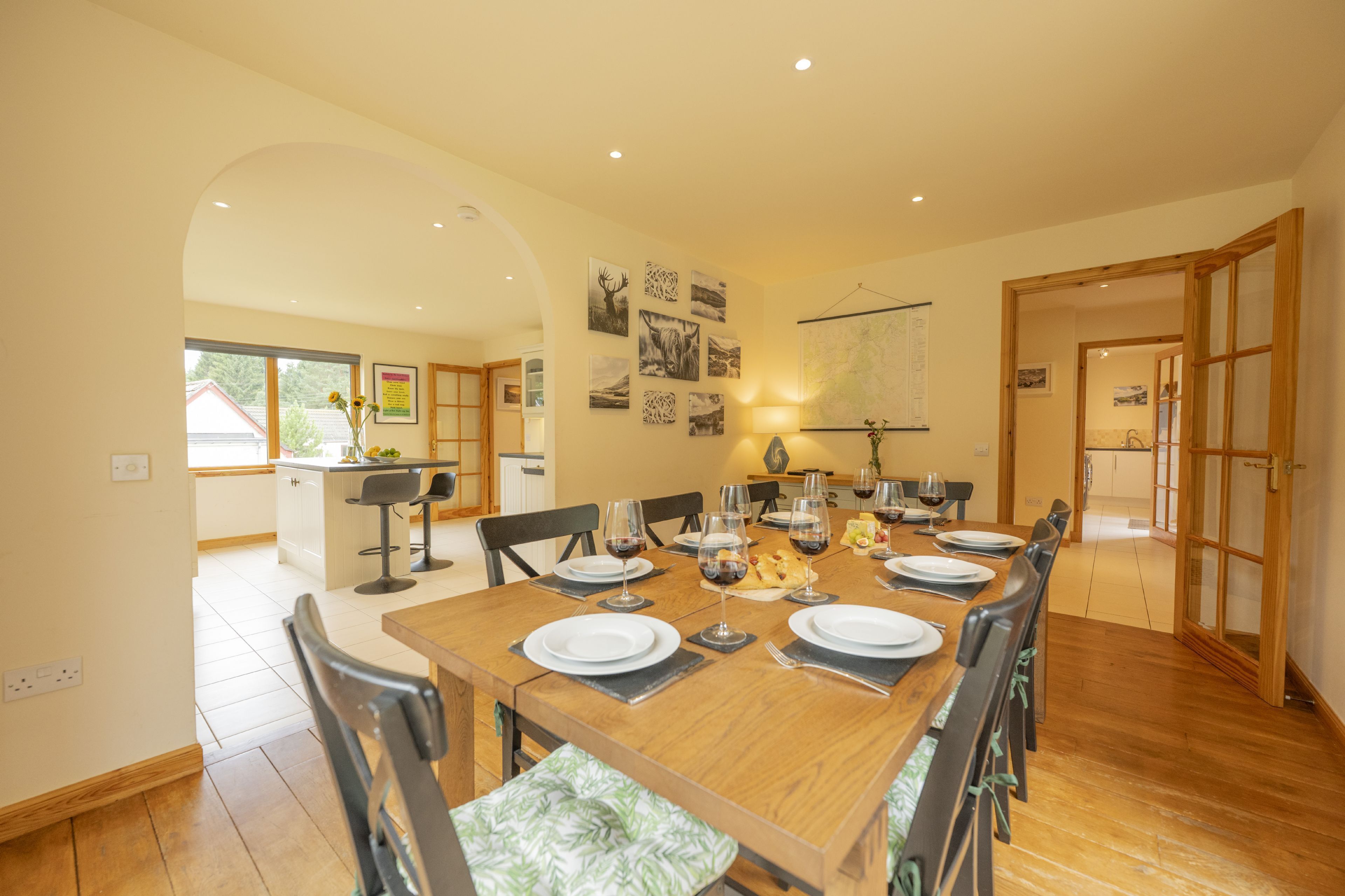Un coin repas avec une table en bois dressée pour six personnes, entourée de chaises dotées de coussins verts.
