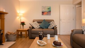 Ein gemütliches Wohnzimmer mit einem braunen Ledersofa, einem Couchtisch mit Kuchen und Keksen, einer Lampe und einem Bild an der Wand.