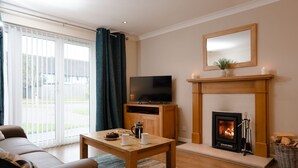 Ein Wohnzimmer mit einer Couch, einem Couchtisch, einem Flachbildfernseher, einem Kamin und einem großen Fenster mit Vorhängen.