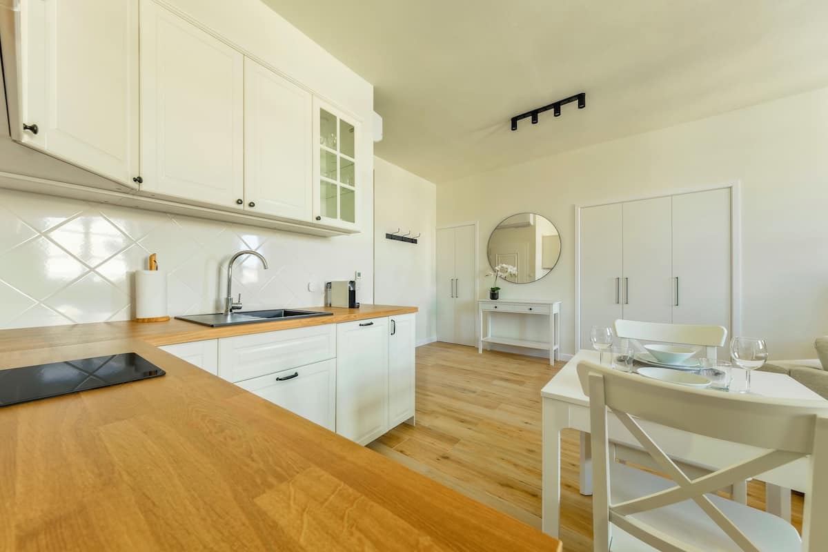 A modern kitchen with white cabinets, a wooden countertop, and a dining area with a white table and chairs.