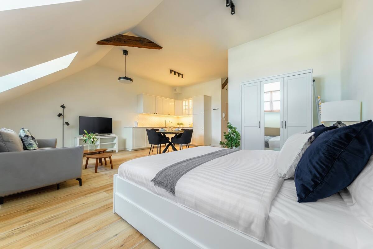 A modern loft bedroom with a large bed, a desk, and a kitchenette.