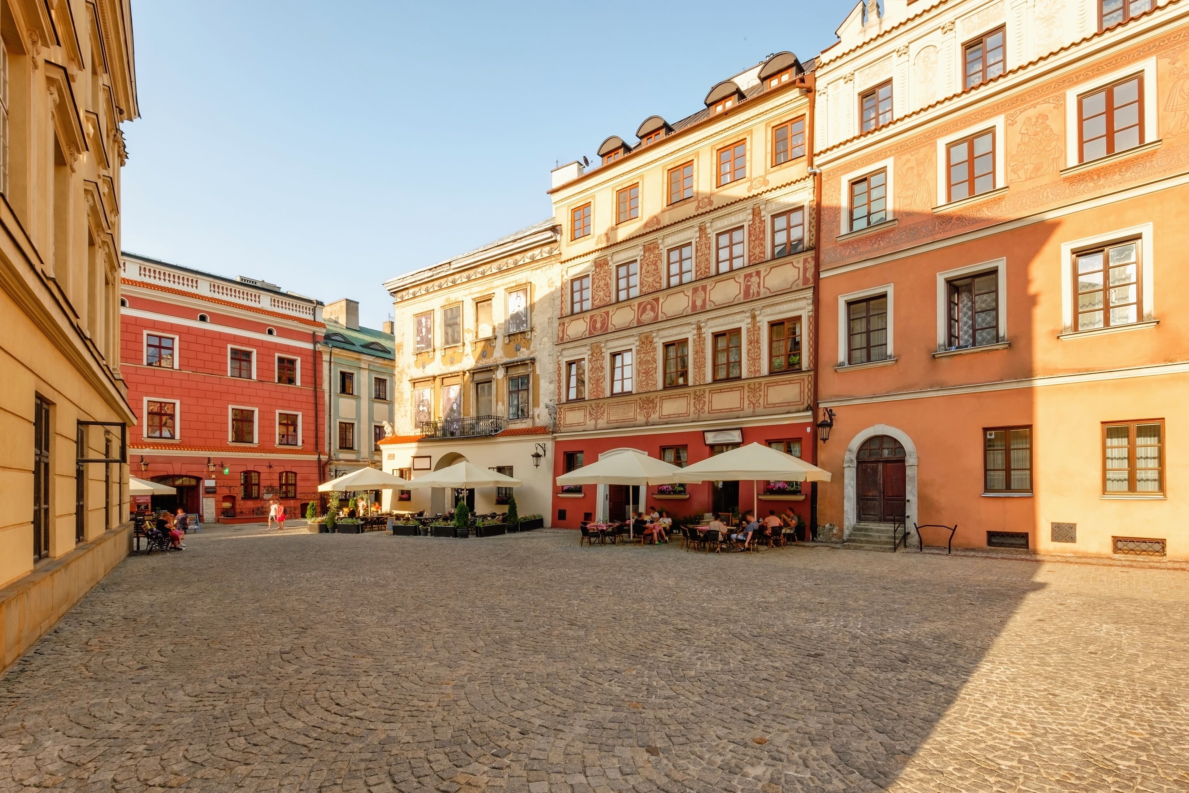 A cobblestone courtyard with outdoor seating areas and buildings with classical architecture.