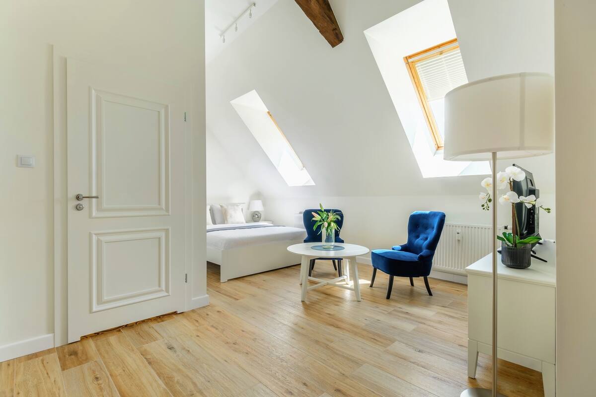 A modern room with a sloped ceiling, a bed, a small round table, two chairs, and a floor lamp.