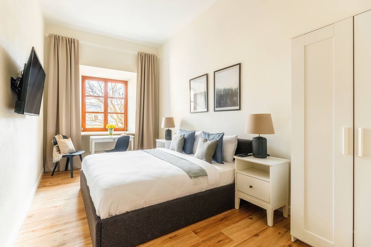 A hotel room with a bed, bedside tables, a desk, a chair, and a wardrobe.