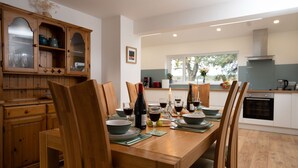 A dining area with a wooden table set for four, surrounded by chairs. A kitchen is visible in the background with modern appliances. - Sleeps 6 in 2 doubles and 1 twin room (Dulnain Bridge)