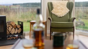 A cozy room with a green armchair, a fireplace, and a view of a forest. - Sleeps 6 in 2 doubles and 1 twin room (Dulnain Bridge)