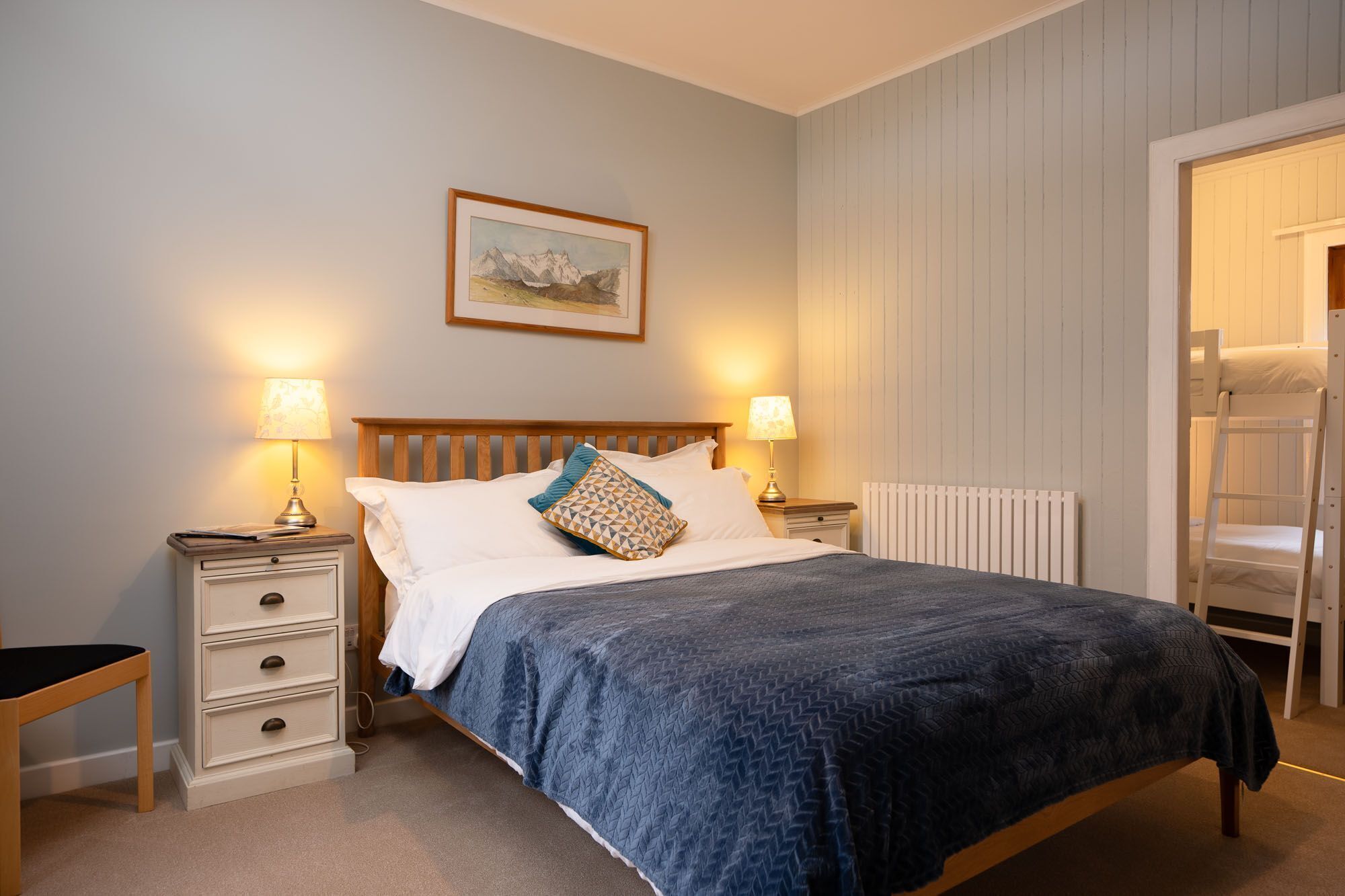 A bedroom with a wooden bed, two bedside tables, a radiator, and a door leading to a loft.
