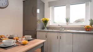A modern kitchen with a wooden table set for breakfast, a refrigerator, and a window with a view.