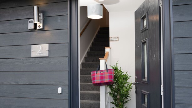 A staircase with a sign instructing to remove shoes before going upstairs, a potted plant, and a red plaid bag hanging on the wall.