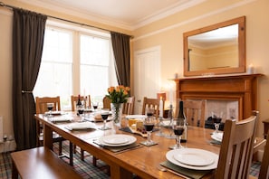 A dining room with a wooden table set for four, a vase with flowers, and a fireplace. - Sleeps 12 in 6 double bedrooms all en-suite (Aviemore)