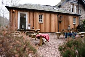A wooden building with a gravel patio, picnic tables, and a door. - Sleeps 12 in 6 double bedrooms all en-suite (Aviemore)