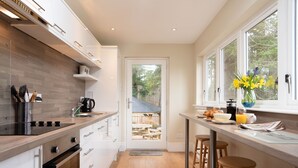 Eine moderne Küche mit Holzarbeitsplatte, weißen Schränken und Blick auf eine Holzdielen-Terrasse durch eine Glastür.