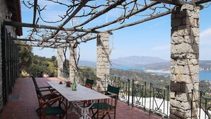 Um terraço com mesa e cadeiras, pilares de pedra e vista para a paisagem.