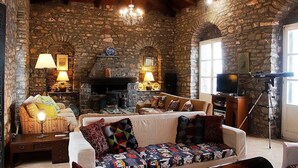 Um quarto rústico com paredes de pedra, lareira, sofá com almofadas estampadas, televisão e um tripé.
