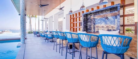 A poolside bar area with blue wicker chairs and a stone wall backdrop.