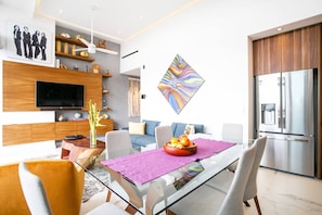 A modern living room with a flat-screen TV, a dining table with a glass top, and a kitchen area with a stainless steel refrigerator. - Luxe Penthouse w/Premium Amenities @ Romantic Zone (Puerto Vallarta)
