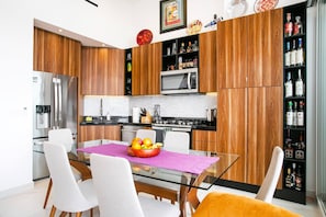 Cocina moderna con armarios de madera, electrodomésticos de acero inoxidable y una mesa de comedor de vidrio con un frutero.