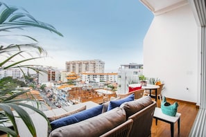 A balcony with a view of a cityscape, furnished with a sofa and chairs, and a small table with a vase. - Luxe Penthouse w/Premium Amenities @ Romantic Zone (Puerto Vallarta)