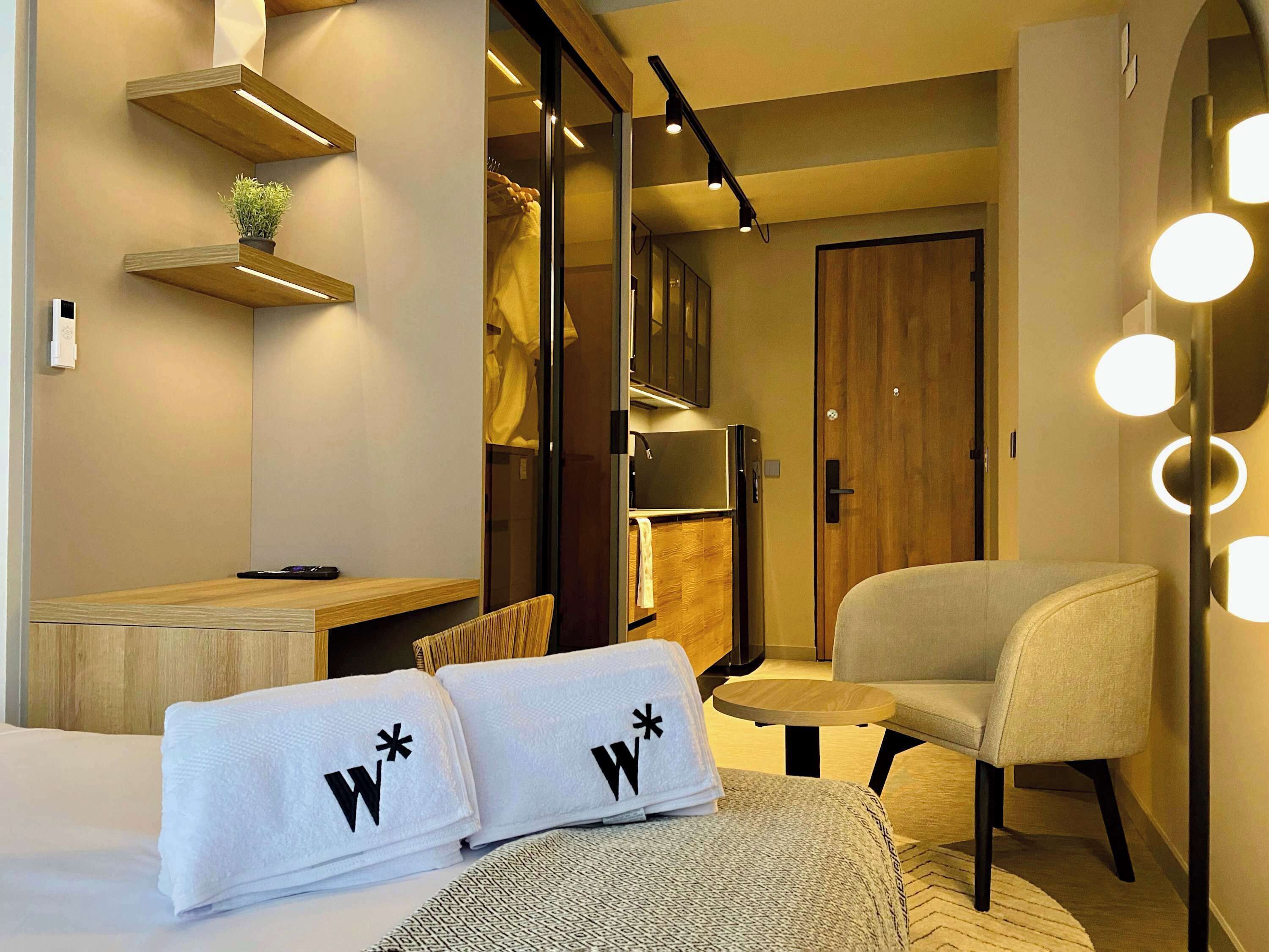 A hotel room with a bed, a chair, a desk, a wardrobe, and a kitchenette.
