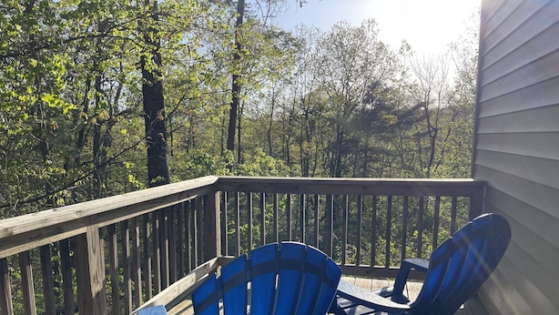 A wooden deck with two blue Adirondack chairs facing a forested area.