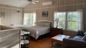 A room with a bed, a desk, a chair, a table, a window, a ceiling fan, and an air conditioning unit.