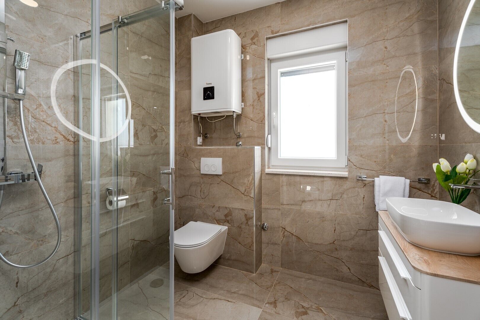 Une salle de bain moderne avec une douche à parois de verre, des toilettes, un lavabo avec un miroir et une fenêtre.