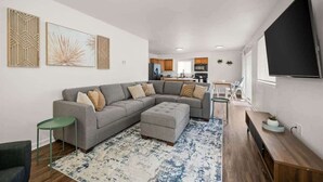 A modern living room with a grey sectional sofa, a small green side table, and a large TV mounted on the wall. - Family Friendly Haven I  Renovated & Spacious! (Spokane Valley)