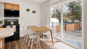 A modern kitchen with a black stove, wooden cabinets, and a dining area with a wooden table and white chairs. - Family Friendly Haven I  Renovated & Spacious! (Spokane Valley)
