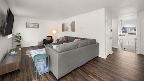 A modern living room with a grey sofa, a small table, and a TV mounted on the wall. - Family Friendly Haven I  Renovated & Spacious! (Spokane Valley)