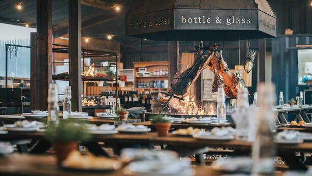 A restaurant with a large wood-fired oven, tables set for dining, and shelves stocked with bottles and glasses. - The Bottle & Glass Inn – Garden View Room 1 (Henley-on-Thames)