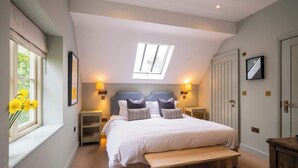 A bedroom with a large bed, a skylight, bedside lamps, a bench, and a wardrobe. - The Bottle & Glass Inn – Garden View Room 1 (Henley-on-Thames)