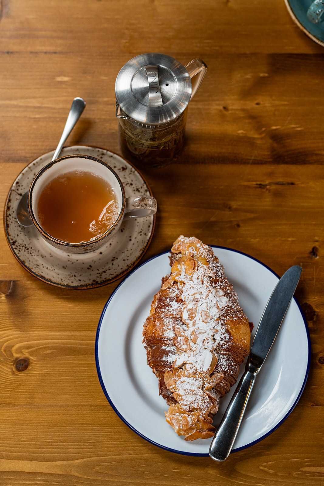 A wooden table with a cup of tea, a teapot, and a plate with a pastry.