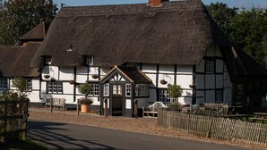 A traditional thatched-roof building with a wooden facade, a central entrance, and a small porch area. - The Bottle & Glass Inn – Barn View Room 2 (Henley-on-Thames)