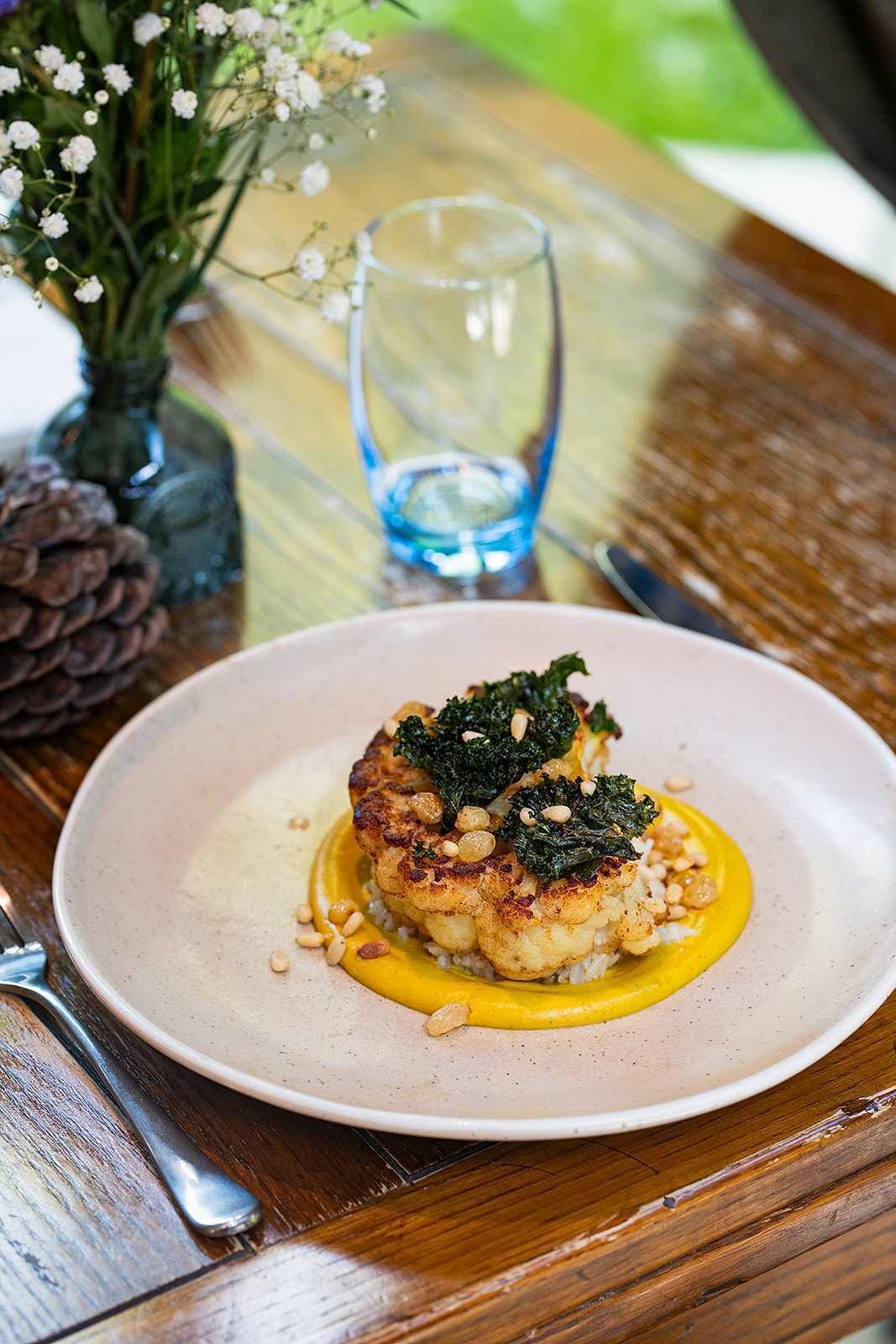 A plate of food on a table with a glass of water and a pine cone in the background.