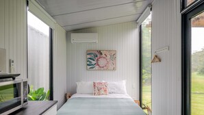 Une chambre à coucher avec un lit, un tableau, un cintre en bois et une fenêtre.