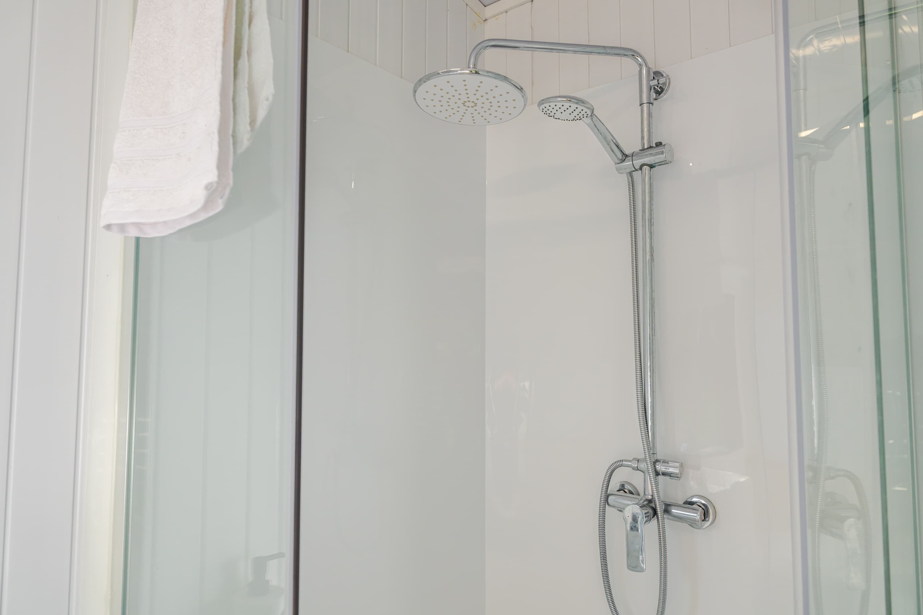 Ducha con cerramiento de vidrio, cabezal de ducha de mano y llave en la pared.