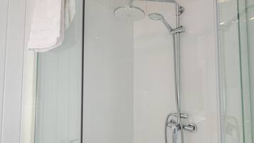 Ducha con cerramiento de vidrio, cabezal de ducha de mano y llave en la pared.