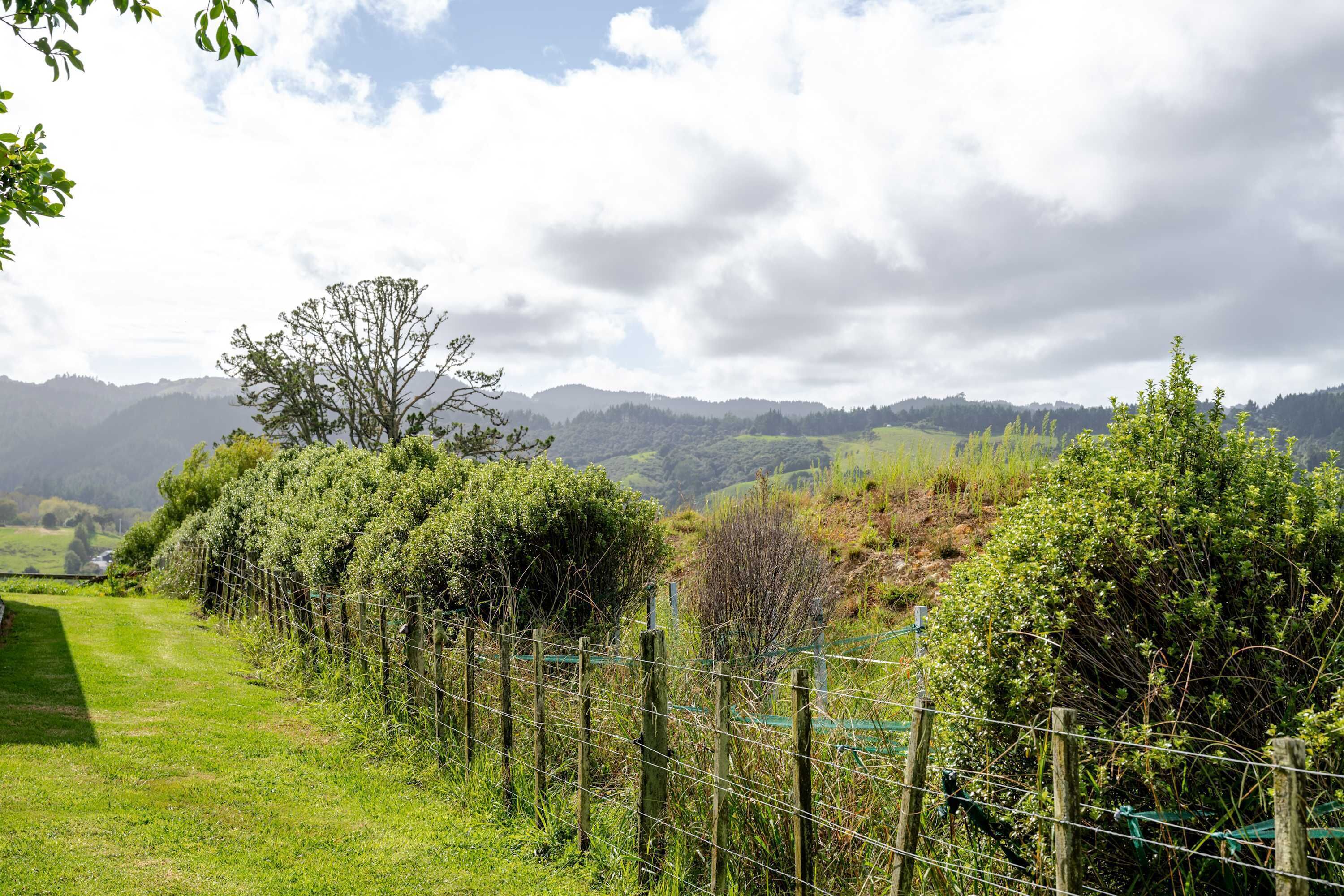 A rural landscape with a fenced path, trees, and distant hills.