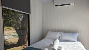 Quarto de hotel com cama, roupa de cama branca, manta verde e vista para uma árvore e grama do lado de fora.