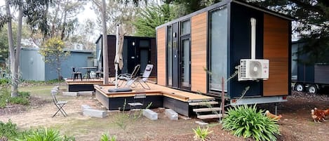 A modern, compact cabin with a deck, outdoor seating, and a large fan.