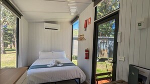 A bedroom with a bed, a desk, a fire extinguisher, and a view of the outdoors. - Tiny House 9 @ Grampians Edge by Tiny Away (Dadswells Bridge)
