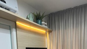 A modern hotel room with a built-in TV, a wooden desk, two green ottomans, and a potted plant on the shelf above the TV. - Flat Itaim SP (São Paulo)