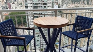 A balcony with two blue woven chairs and a small round wooden table. - Flat Itaim SP (São Paulo)