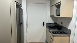 A compact kitchen with a refrigerator, stove, and microwave. - Flat Itaim SP (São Paulo)