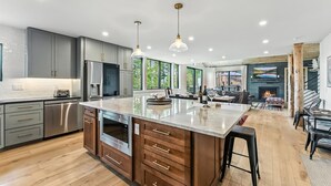 A modern kitchen with stainless steel appliances, wooden cabinets, and a large island with stools. - Ski-In/Ski-Out Breckenridge Retreat with Hot Tub (Breckenridge)