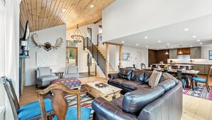 A spacious living area with a leather sofa, wooden chairs, a staircase, and a dining area with a kitchen in the background. - Ski-In/Ski-Out Breckenridge Retreat with Hot Tub (Breckenridge)