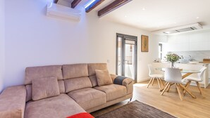 En moderne stue med en beige sofa, et rødt plaide og et spiseområde med et glasbord og hvide stole.
