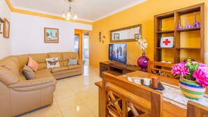 Una sala de estar con sofá, televisor, mesa de madera y repisas con adornos.