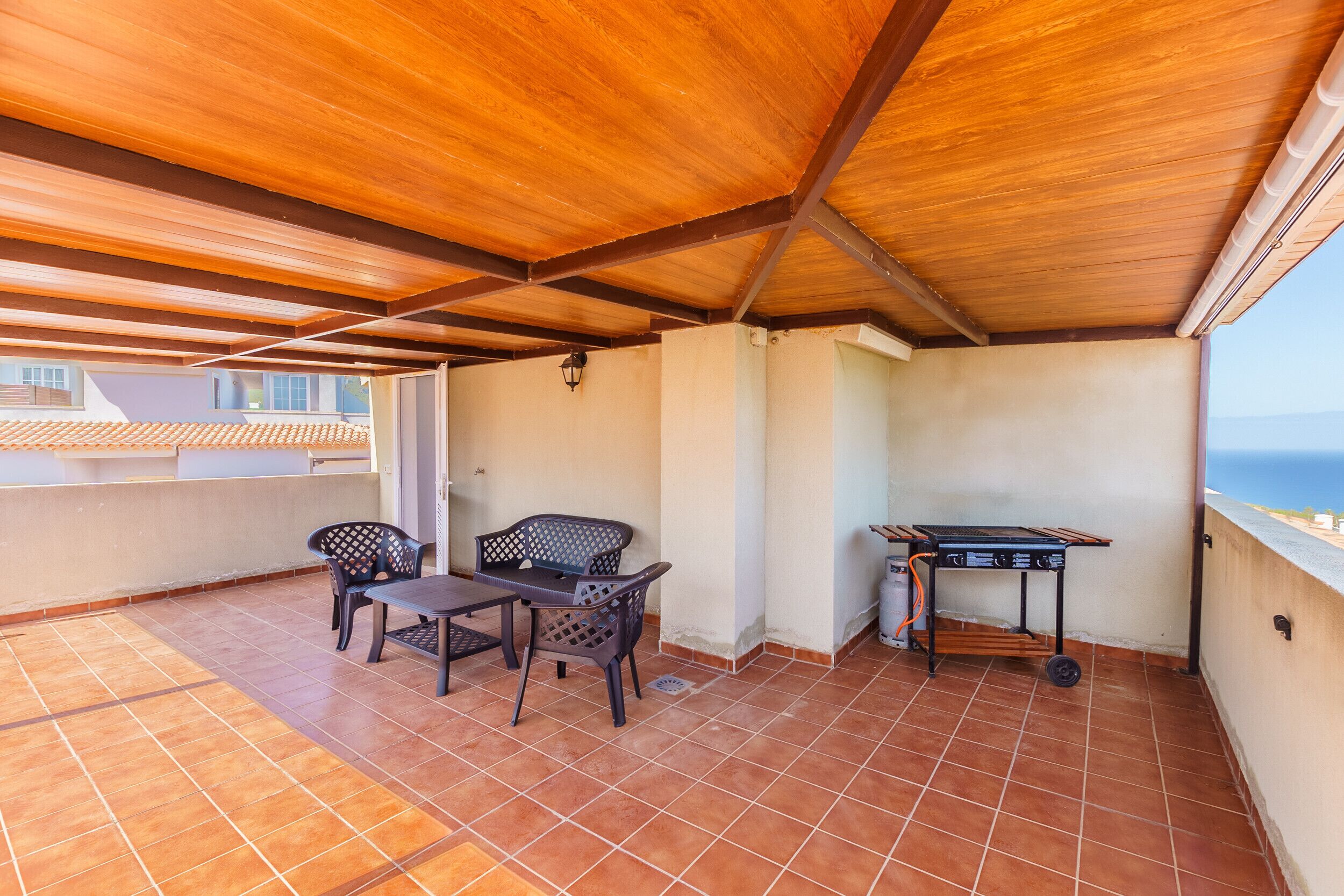 A covered outdoor patio with a wooden ceiling, tiled floor, and a table with chairs.